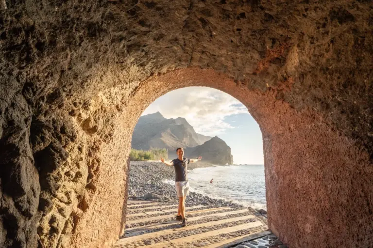 Jonathan am felsigen Tunneleingang an der Küste Gran Canarias, mit den Bergen im Hintergrund.