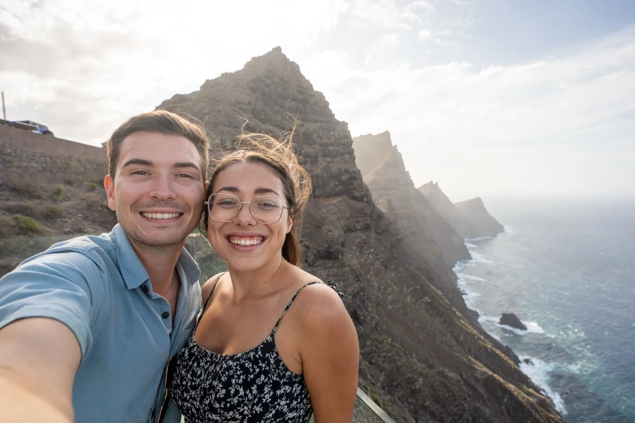 Clara und Jonathan auf einer Klippe auf Gran Canaria, Meereswellen und felsige Berge im Hintergrund.
