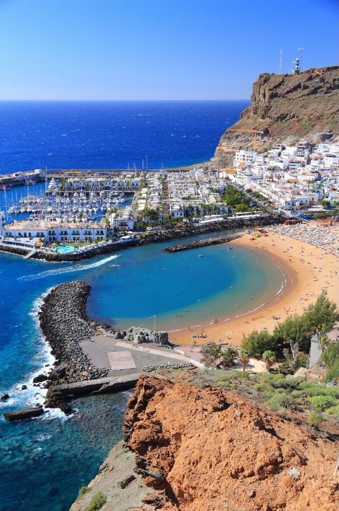 Luftaufnahme des Sandstrandes Playa Anfi de Mar auf Gran Canaria, des Jachthafens, der Stadt, des blauen Meeres und der felsigen Klippen.