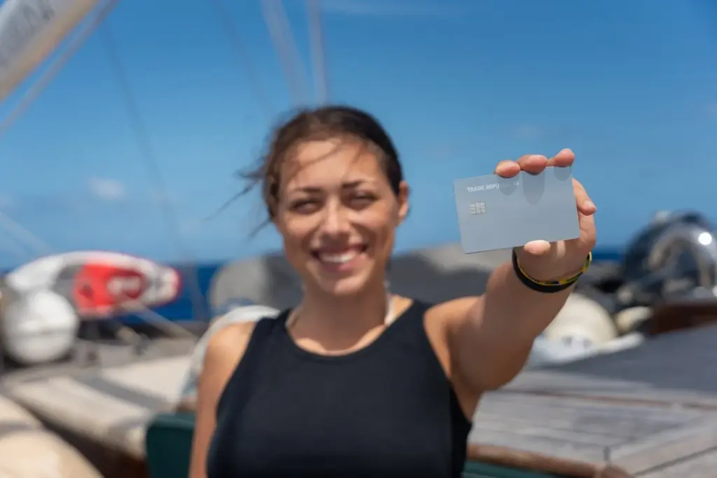 Clara hält die silberne Trade Republic Karte in ihrer Hand auf einem Segelboot.