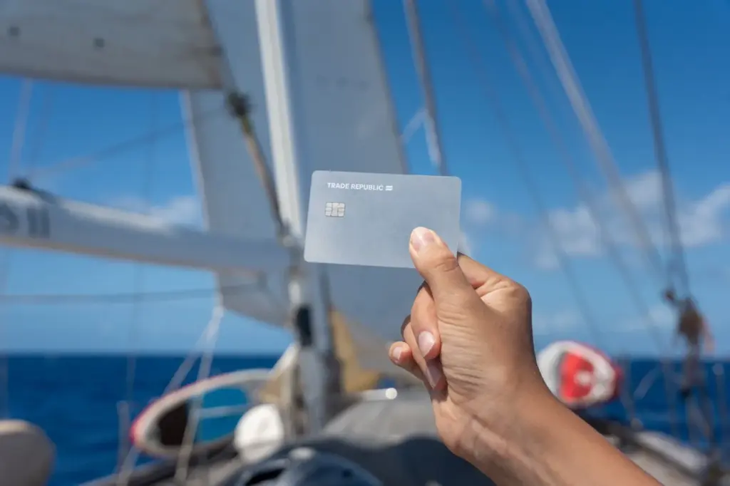 Die Trade Republic Karte als kostenlose Debitkarte für Reisen auf einem Segelboot und unter blauem Himmel. 