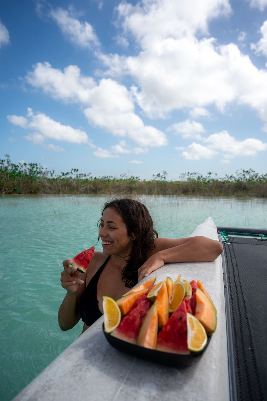 Frau isst Wassermelone im tuerkisen Wasser der Lagune von Bacalar am Katamaran