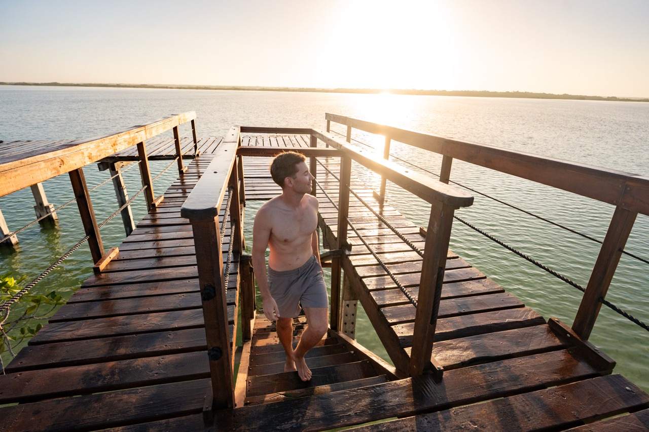 Mann auf einem Holzsteg an der Lagune von Bacalar im Gegenlicht