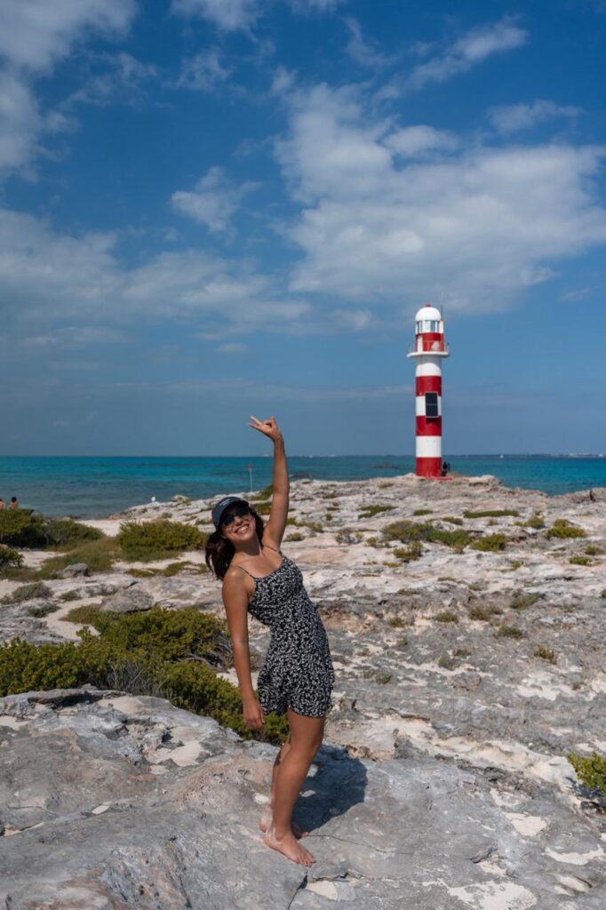 Frau posiert vor dem rot-weissen Leuchtturm an der Felskueste von Cancun
