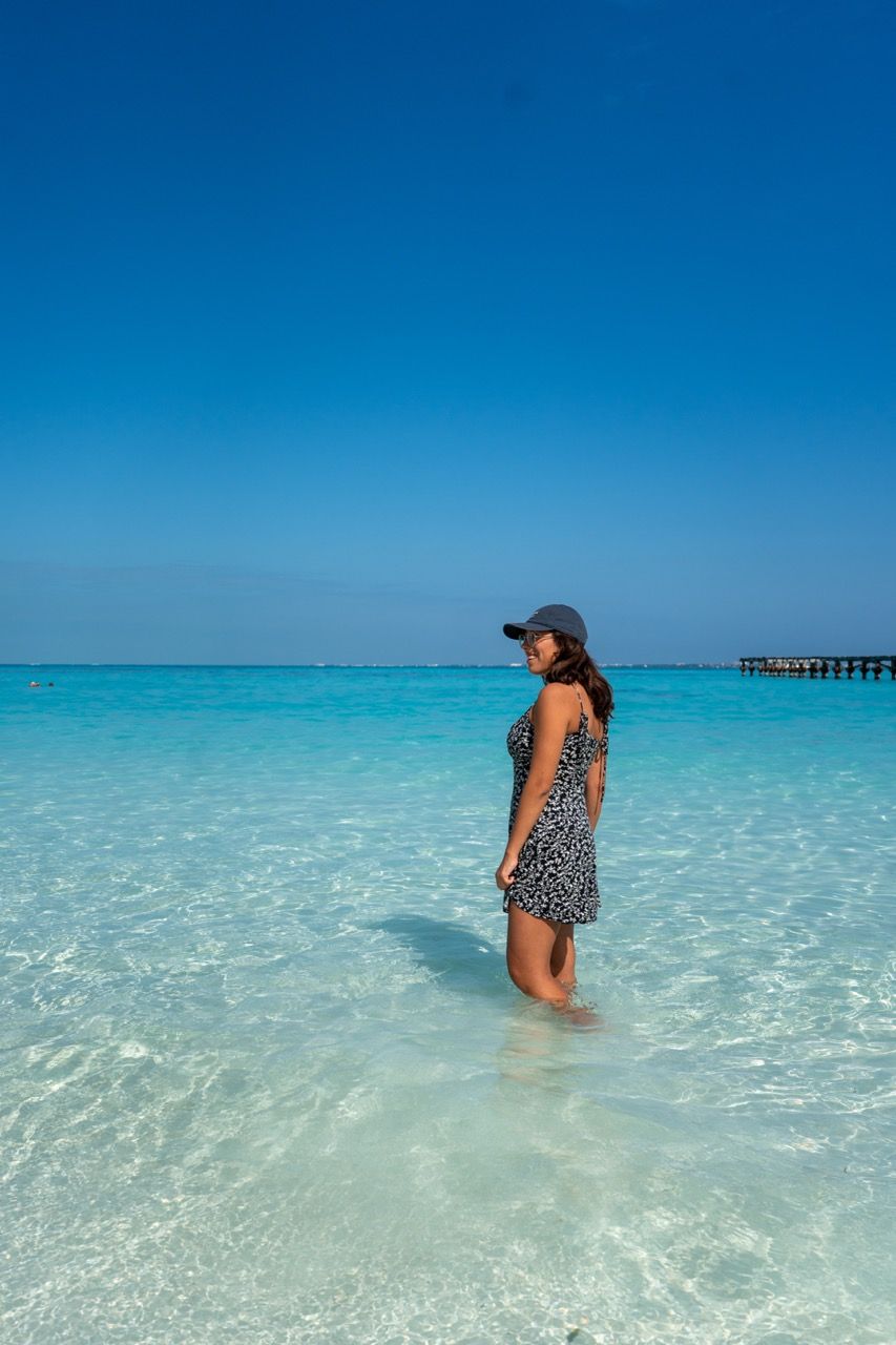 Frau steht im klaren tuerkisfarbenen Wasser am Strand von Cancun mit Seebruecke