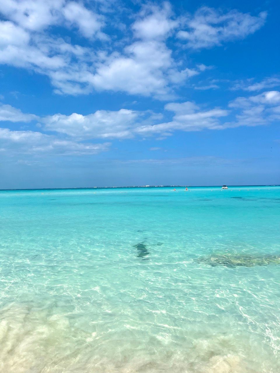 Kristallklares tuerkises Meer vor Cancun mit Boot am Horizont und wolkigem Himmel