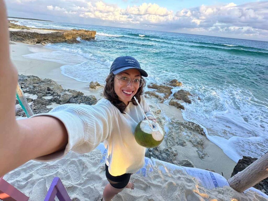 Laechelnde Frau mit Kokosnuss am felsigen Strand von Cozumel