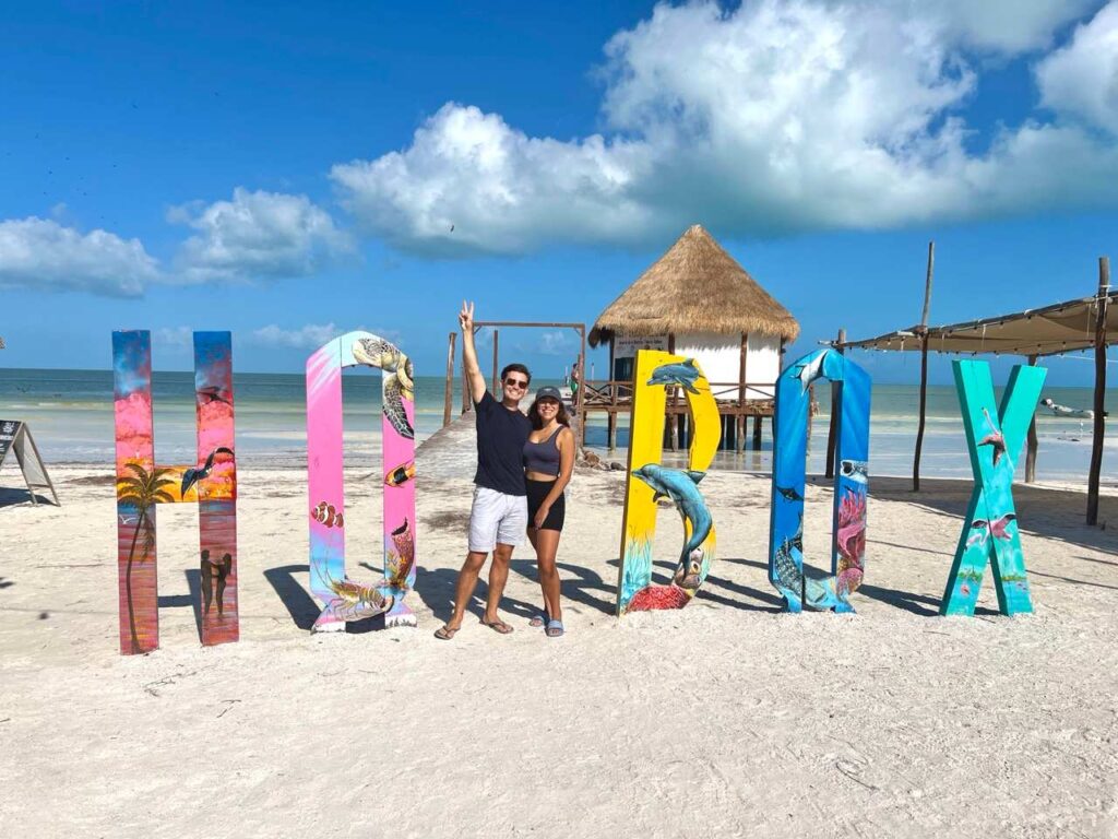Paar vor dem bunten HOLBOX-Schriftzug am Strand von Holbox