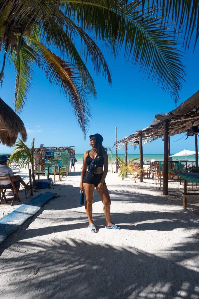 Frau steht unter einer Palme am Strand von Holbox