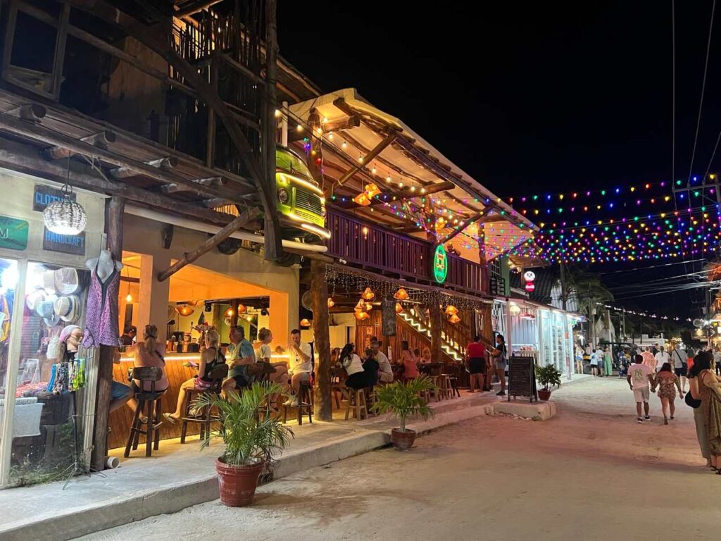 Belebte Sandstrasse in Holbox bei Nacht mit Bar und bunten Lichterketten