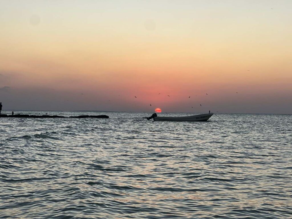 Sonnenuntergang ueber dem Meer vor Holbox mit ankerndem Fischerboot und Voegeln