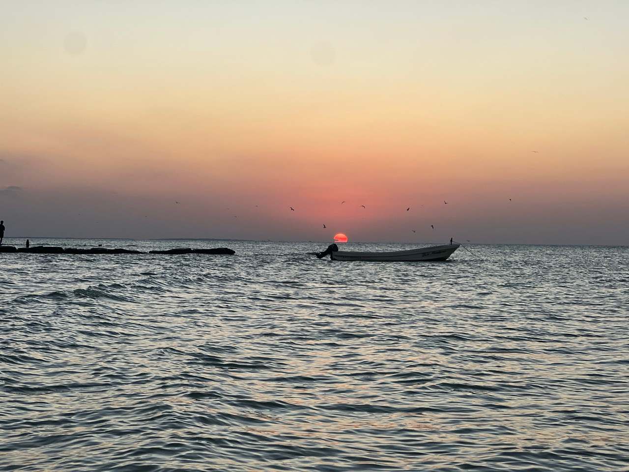 Sonnenuntergang ueber dem Meer vor Holbox mit ankerndem Fischerboot und Voegeln