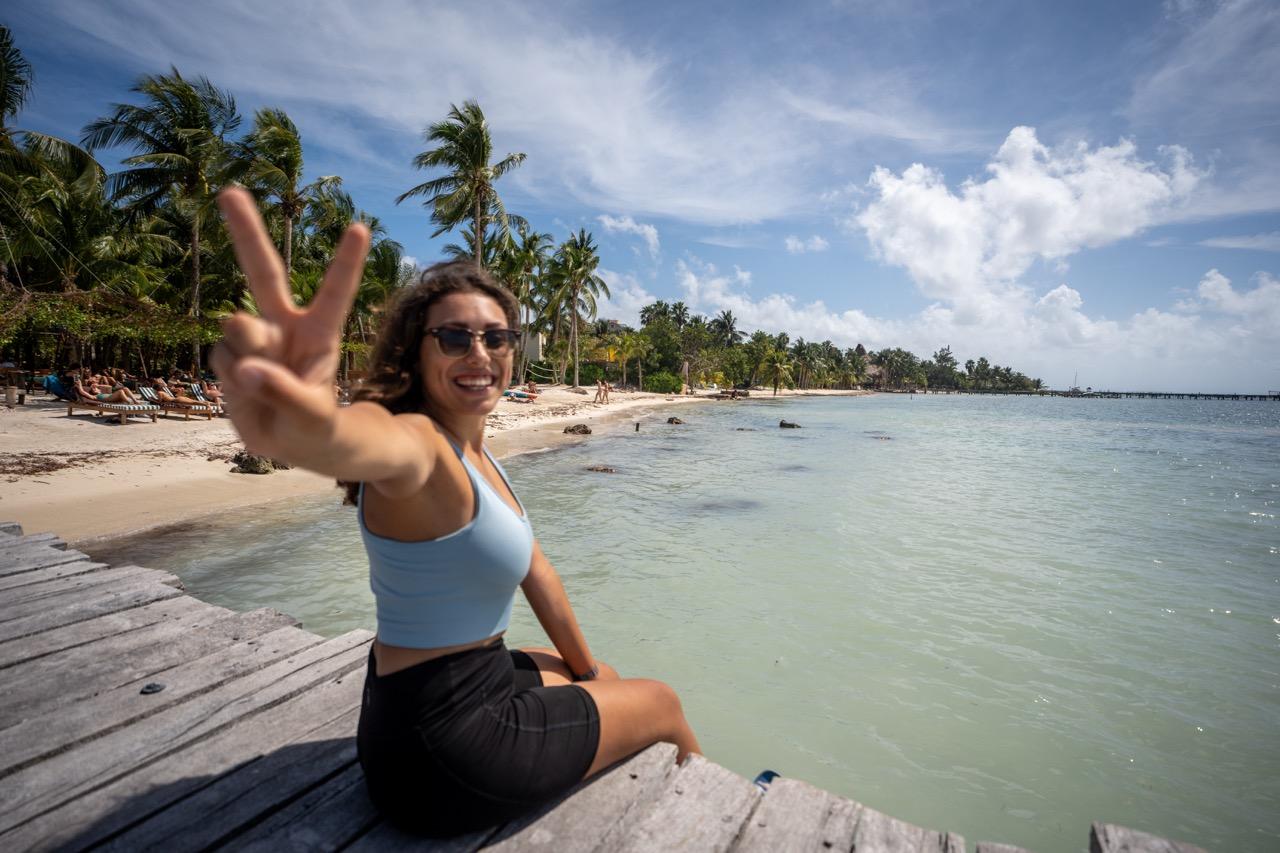 Mexiko beste Reisezeit: Frau sitzt am Holzsteg von Holbox vor tuerkisem Wasser und Palmenstrand