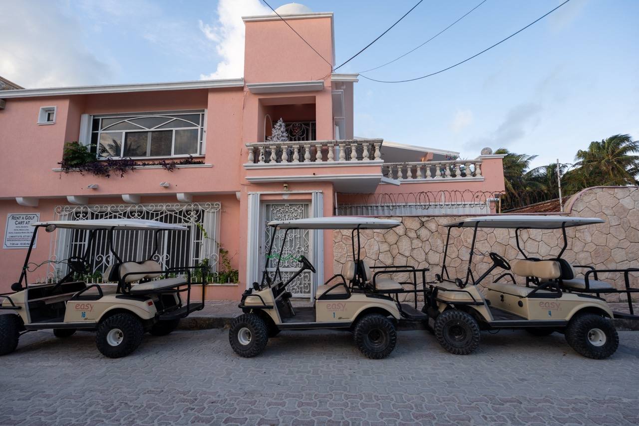 Golf-Carts vor rosa Haus in einer Strasse auf Isla Mujeres