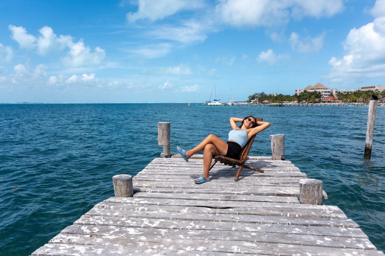 Frau entspannt auf Holzsteg ueber tuerkisem Wasser auf Isla Mujeres