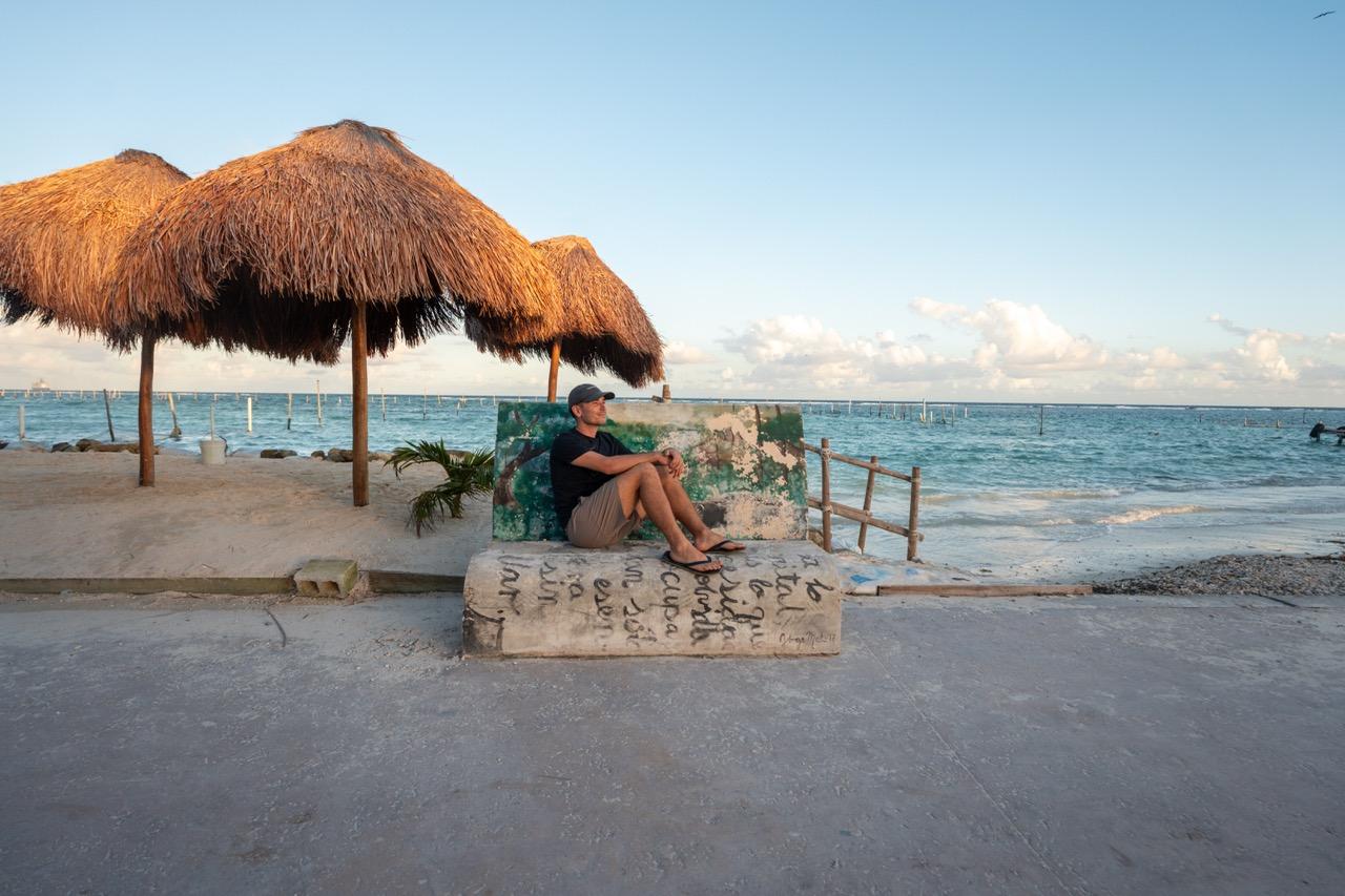 Mann sitzt bei Sonnenuntergang unter Palapas am Strand in Mahahual