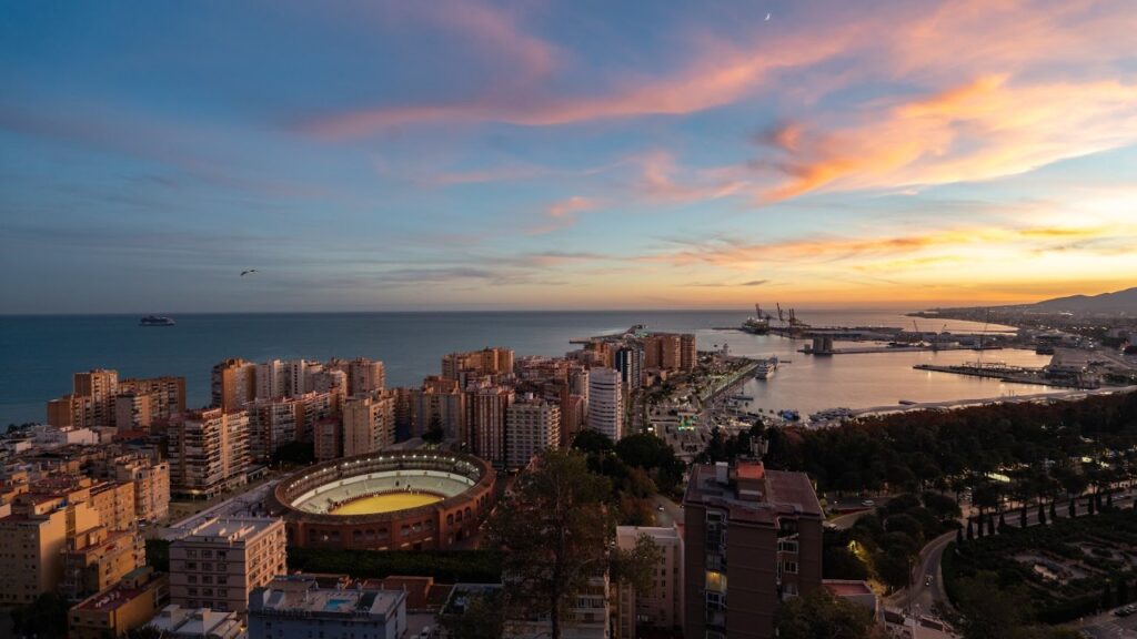 Blick über Málaga mit Stierkampfarena und Hafen bei Sonnenuntergang
