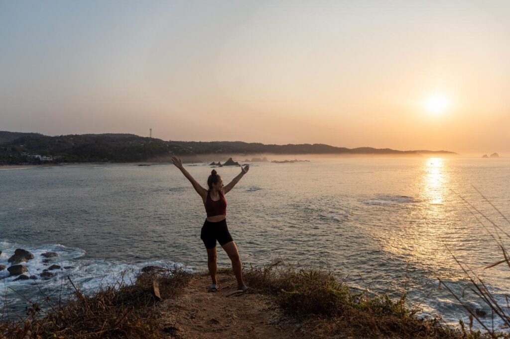 Frau mit erhobenen Armen auf Klippe bei Sonnenuntergang in Mazunte