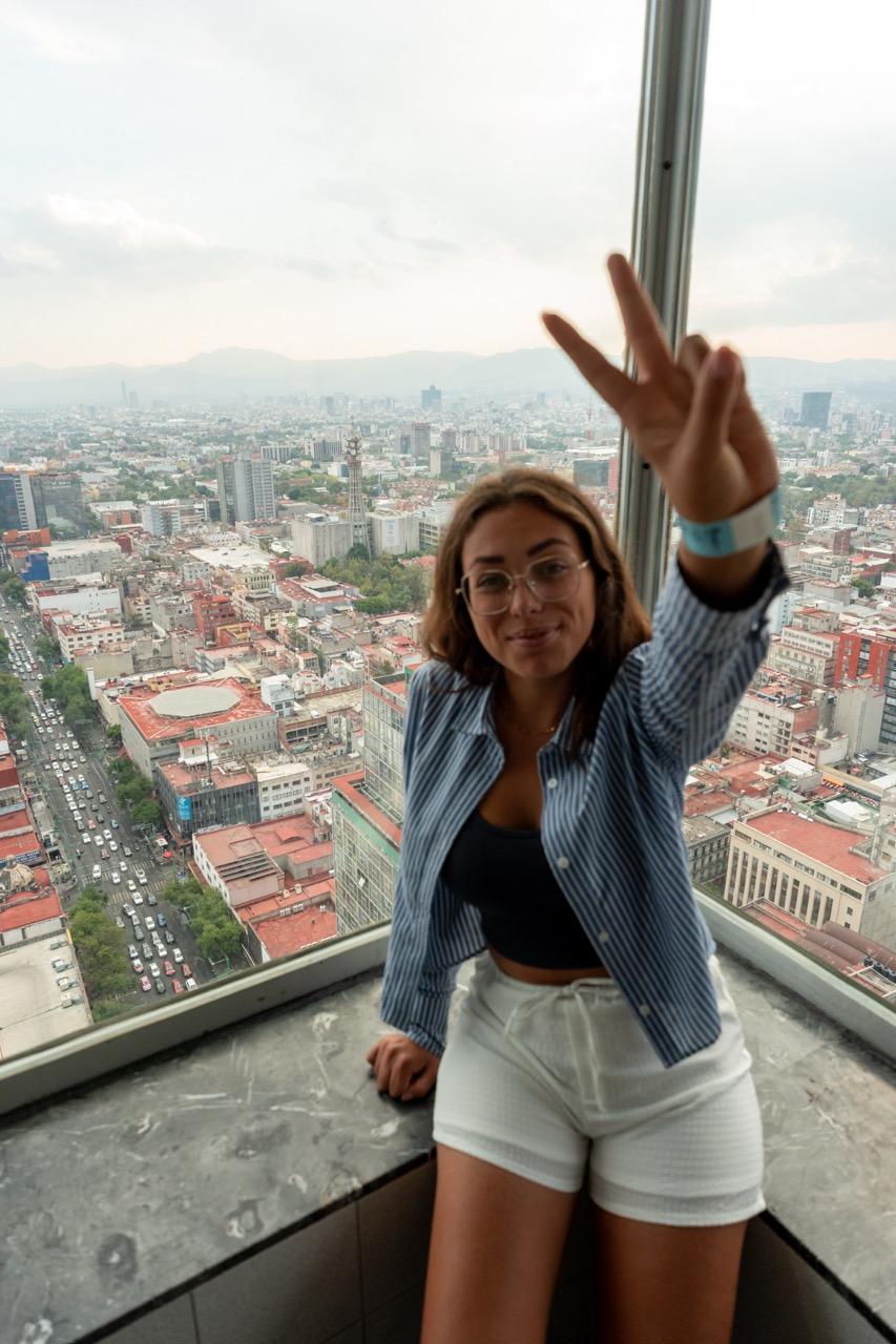 Frau mit Peace-Zeichen vor dem Panorama von Mexico City