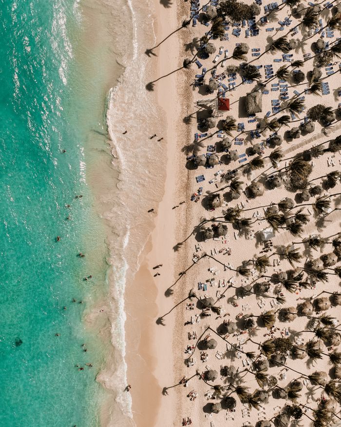 Stunning drone shot capturing beachgoers on a vibrant tropical beach with clear turquoise waters and palm trees.