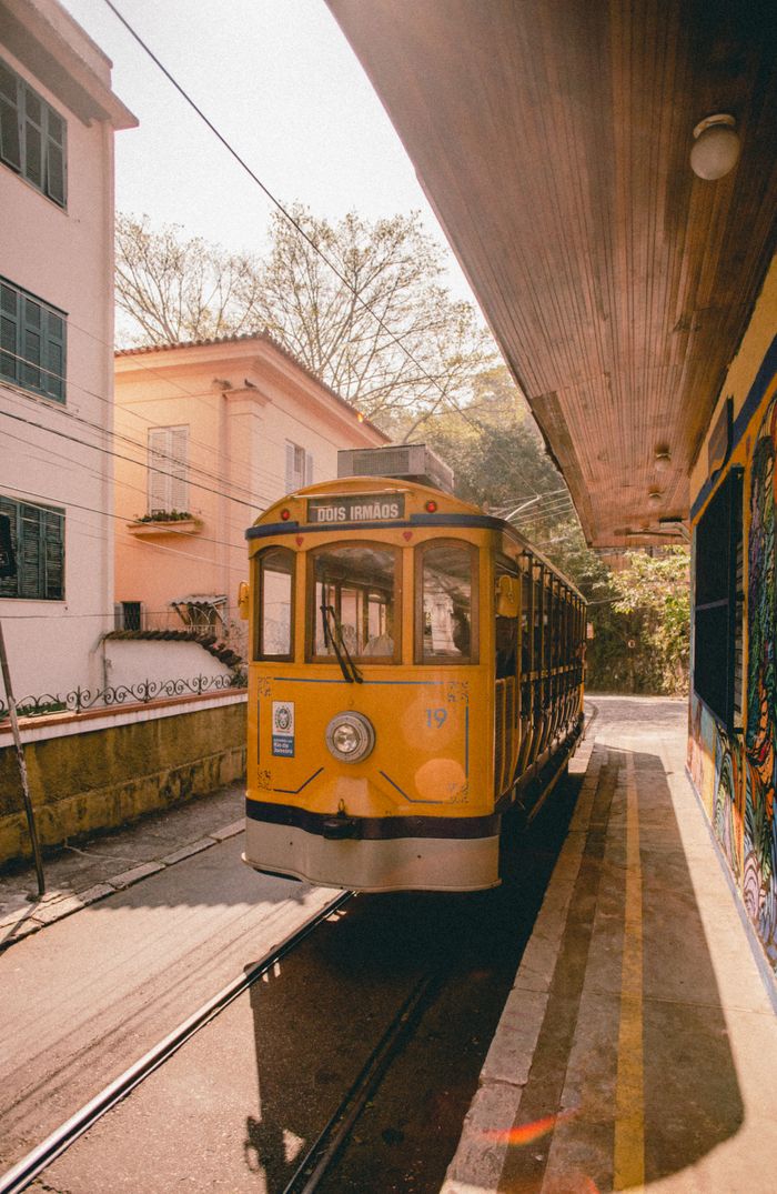 A classic yellow tram parked at a station surrounded by residential buildings on a sunny day.