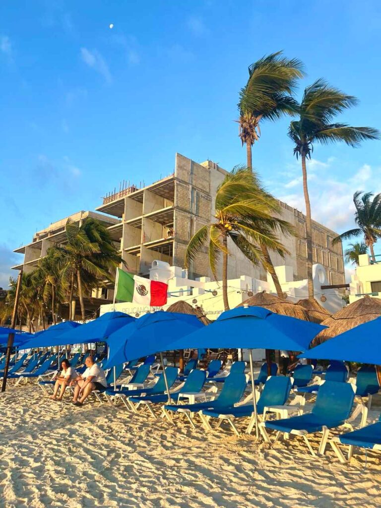 Blaue Sonnenschirme und Liegen am Strand von Playa del Carmen mit Palmen