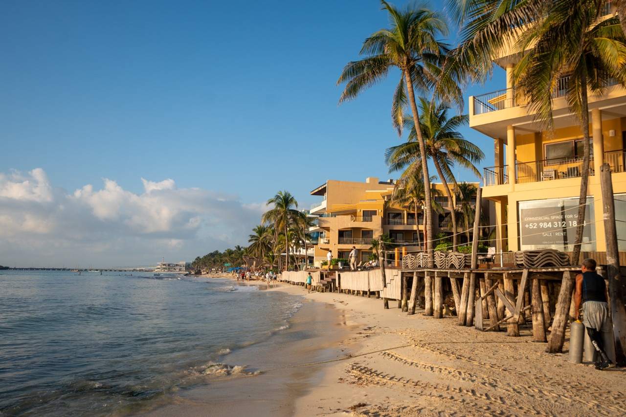 Sandstrand mit gelben Hotelgebaeuden und Palmen am Meer in Playa del Carmen