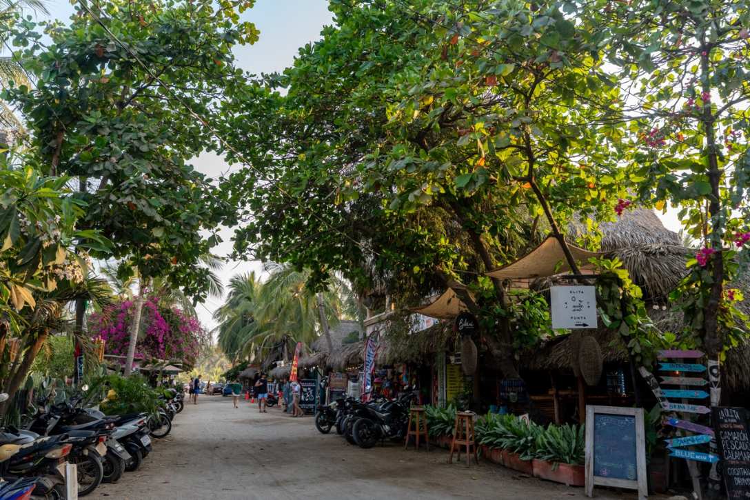 Sandstrasse mit Restaurants und Baeumen in Puerto Escondido