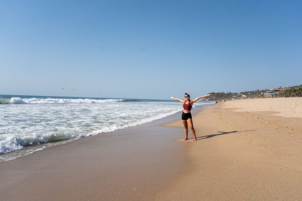 Frau mit ausgebreiteten Armen am breiten Sandstrand von San Pancho bei Wellen