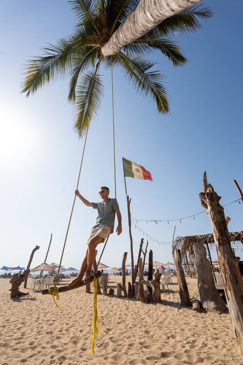 Mann sitzt auf einer Palmenschaukel am Strand mit mexikanischer Flagge in San Pancho