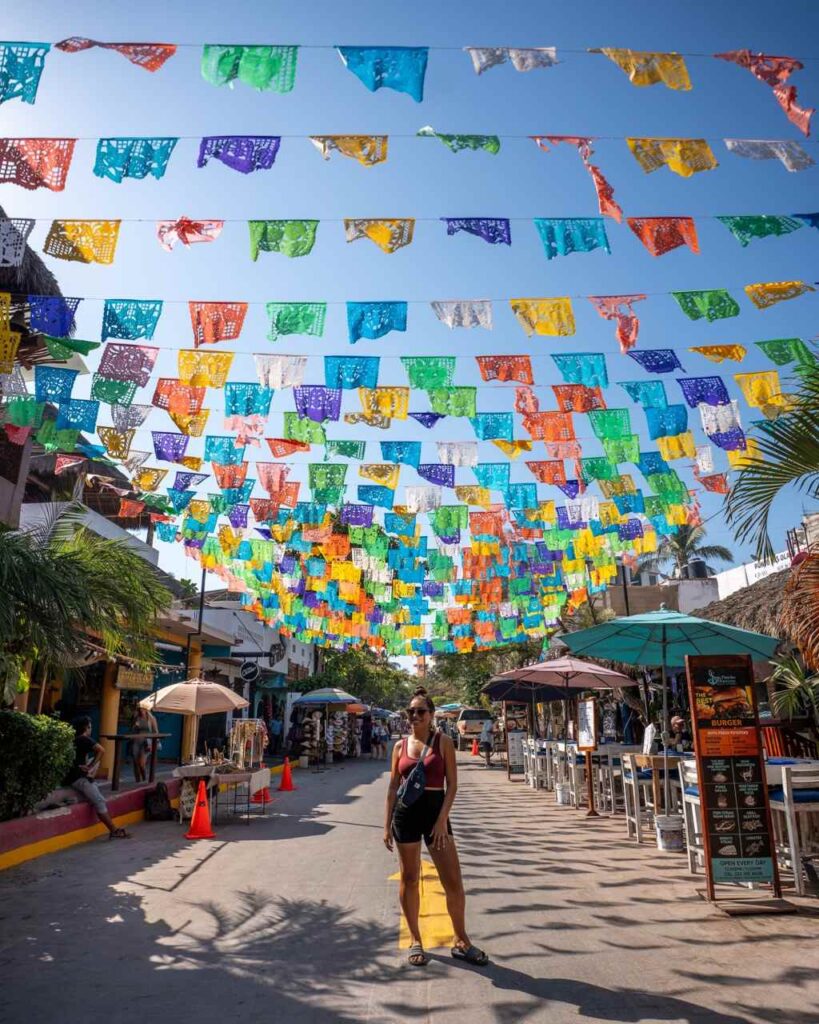 Frau steht unter bunten Papel-Picado-Wimpeln in einer Gasse in Sayulita
