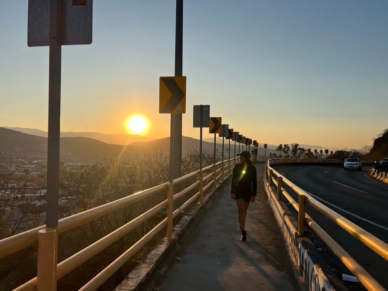 Person geht bei Sonnenuntergang ueber einen Fussweg mit Blick auf Oaxaca