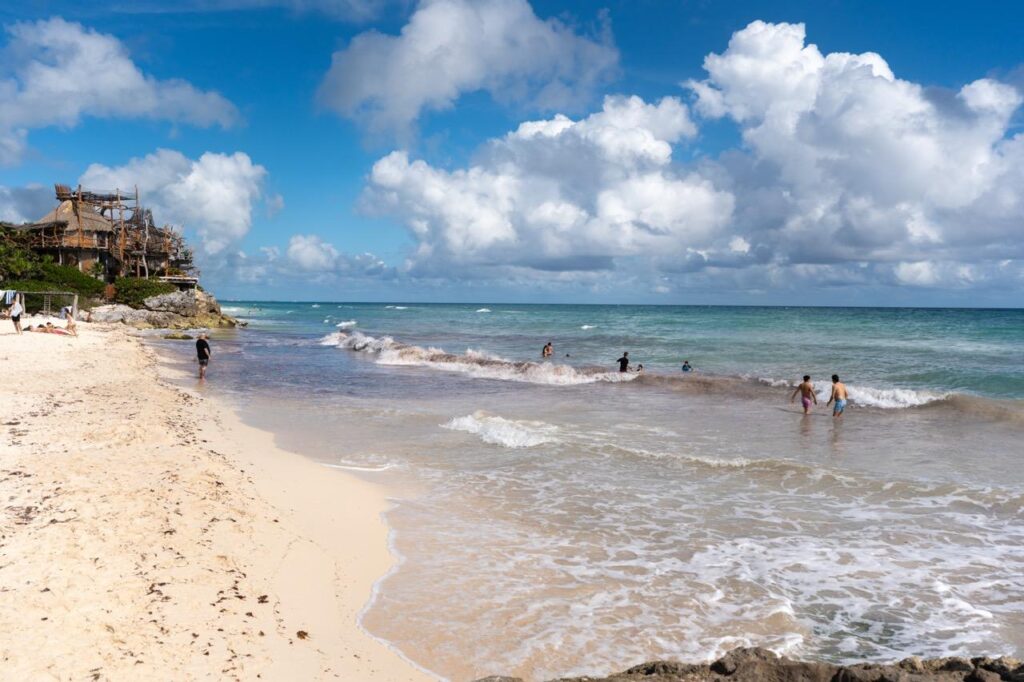 Badegaeste am tuerkisen Strand von Tulum mit Palapa auf der Klippe