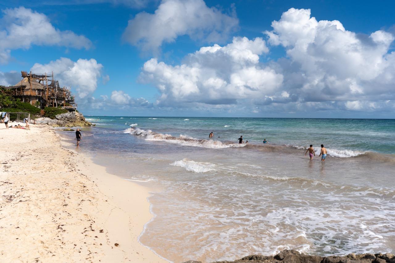 Badegaeste am tuerkisen Strand von Tulum mit Palapa auf der Klippe