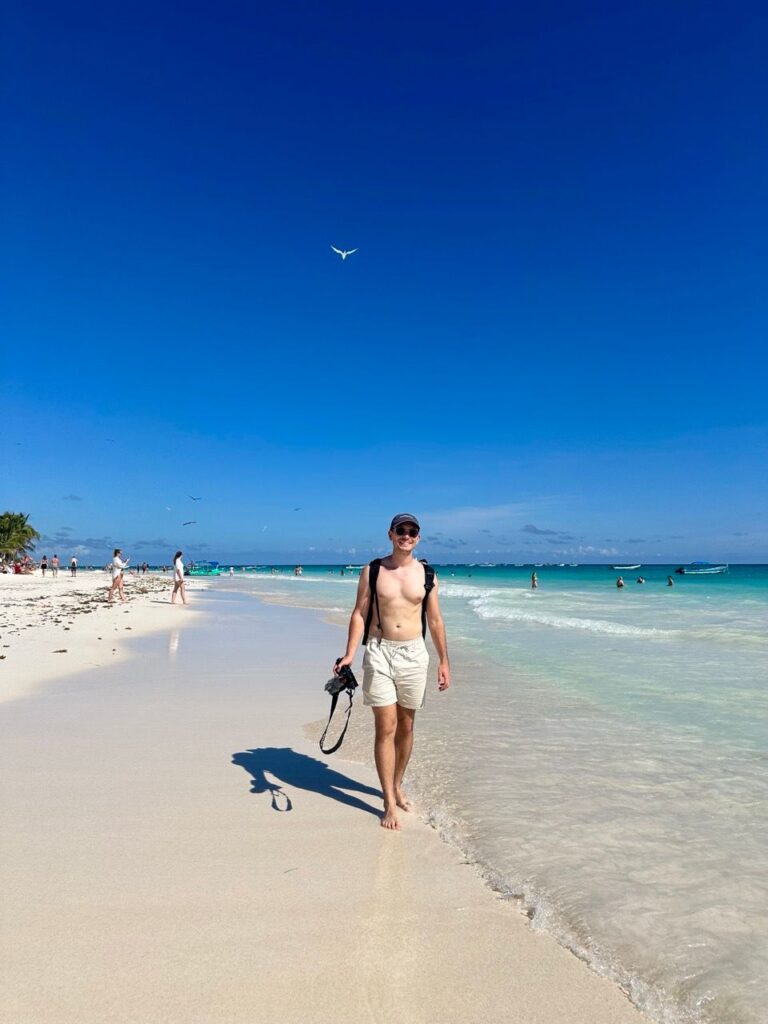 Mann spaziert am tuerkisen Strand von Tulum, Vogel am Himmel