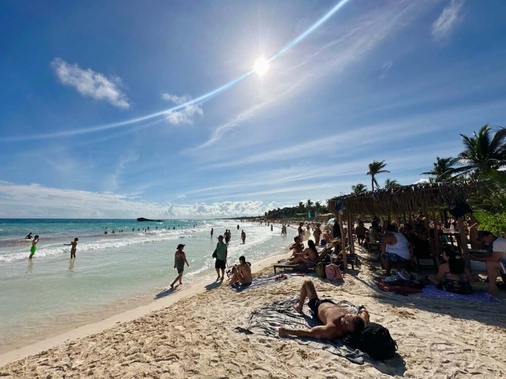 Belebter Strand von Tulum mit Badegaesten, Palmen und strahlender Sonne
