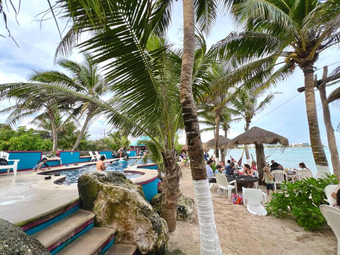Strandclub mit Pool, Palmen und Gaesten am Meer in Tulum