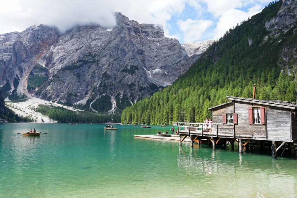 A serene view of a mountain lake with a wooden cabin, boats, and lush forest.