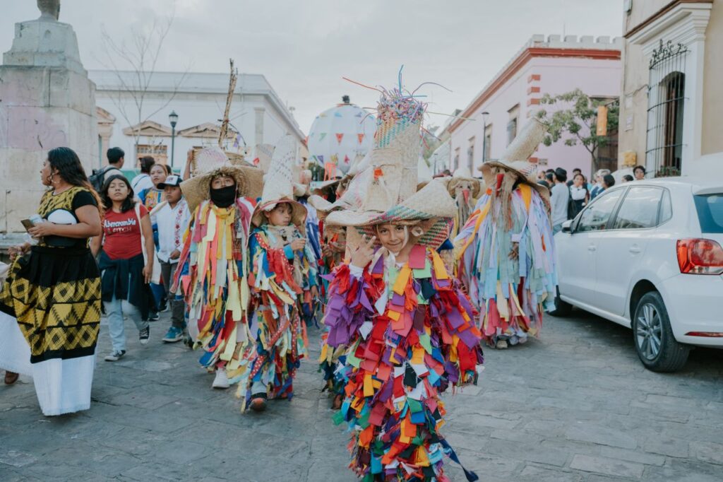 Vibrant traditional parade with participants in colorful costumes on a street in Oaxaca, Mexico.